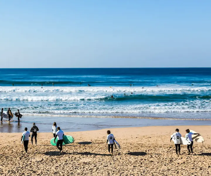 Aulas de Surf em Grupo | Gecko Surf School – Costa da Caparica Grupo de alunos a surfar uma onda na Costa da Caparica durante uma aula de surf em grupo da Gecko Surf School